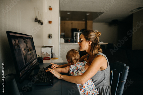 Multitasking working mother holding baby and typing on computer