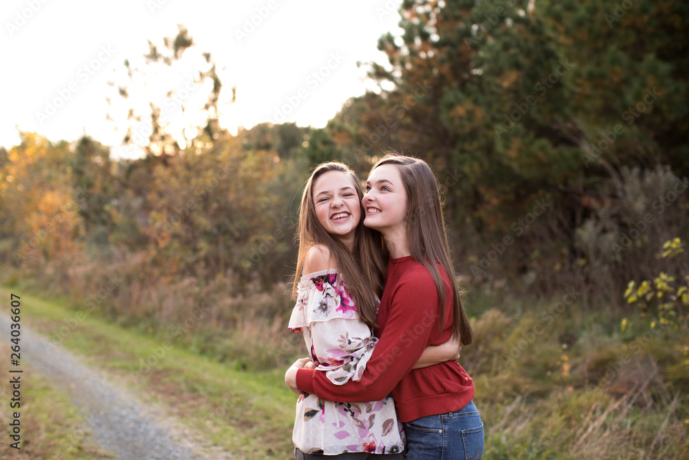 Teen Sisters Happily Hugging and Laughing on Trail at Sunset in Fall Teen Sisters Happily Hugging and Laughing on Trail at Sunset in Fall