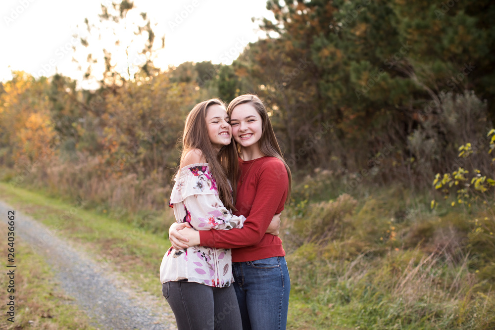 Teenage Sisters Happily Hug Each Other, Standing on Trail at Sunset Teenage Sisters Happily Hug Each Other, Standing on Trail at Sunset