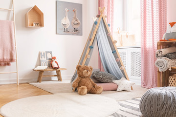 Teddy bear and star pillow in front of tent in child's room interior with pouf and poster. Real photo