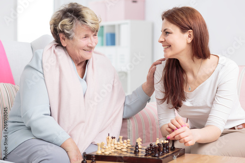 Happy granddaughter playing chess with her grandmother in senior care center