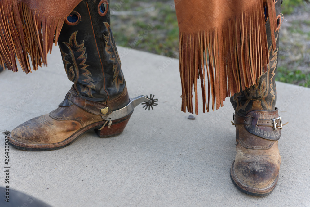 Old cowboy boots are weathered and brown with stitched design on the side  with spurs worn by an old cowboy in jeans. Photos | Adobe Stock