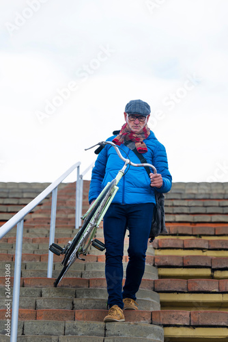 Senior man carrying bicycle while going down stairs against cloud sky photo