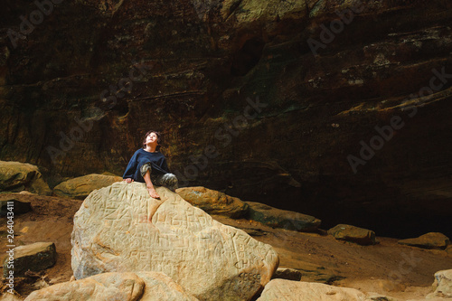 A small boy sits barefoot on a golden rock surrounded by cliff walls photo