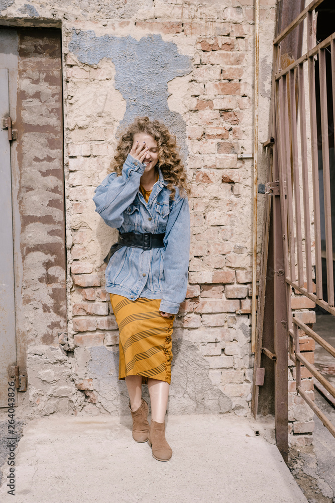Young beautiful curly woman stands near wall in a retro dress Young beautiful curly woman stands near wall in a retro dress