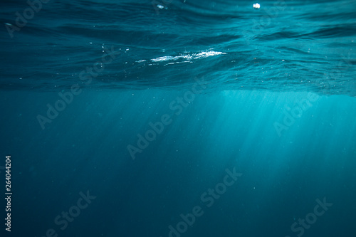 An underwater view of sun rays penetrating surface of blue ocean