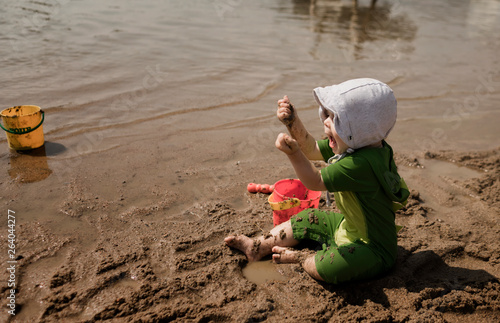 Little girl in bonnet playing with brother at the beach
