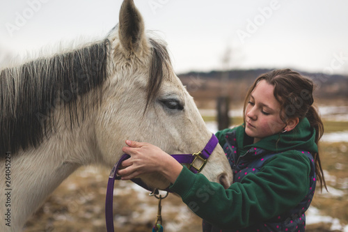 teen girl putting halter on white horse