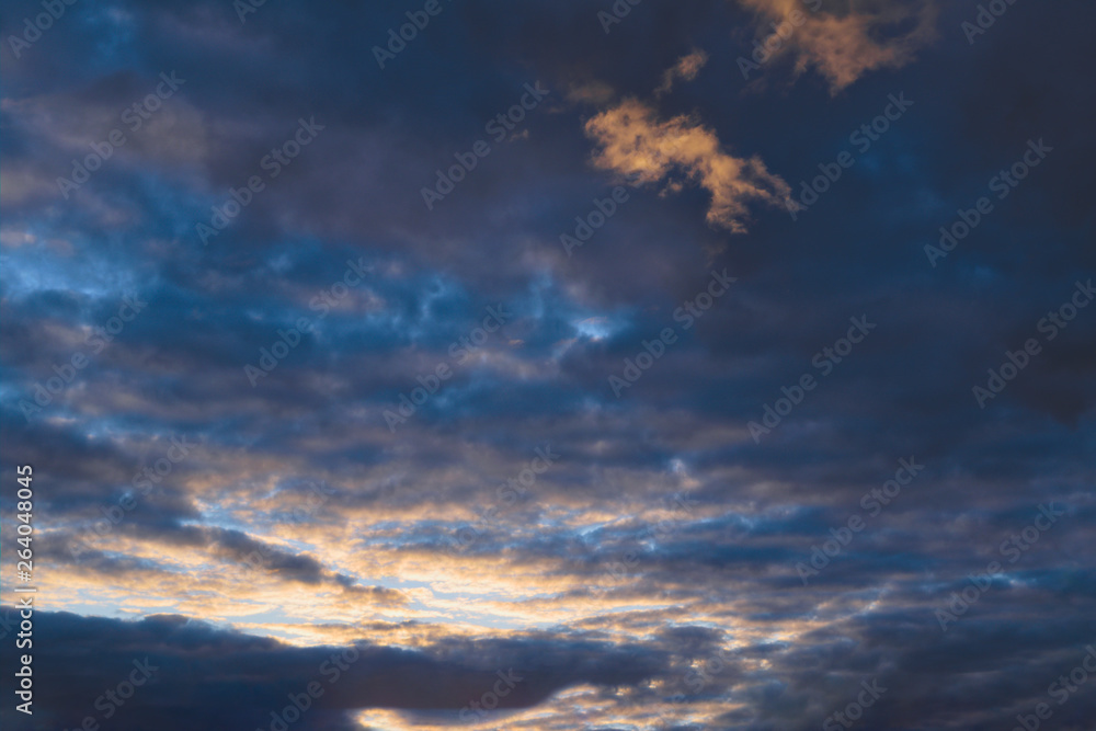 Blue sky with gold clouds - dramatic sunset, beautiful natural background. Setting sun illuminates the clouds. Blue sky with gold clouds - dramatic sunset, beautiful natural background. Setting sun illuminates the clouds.