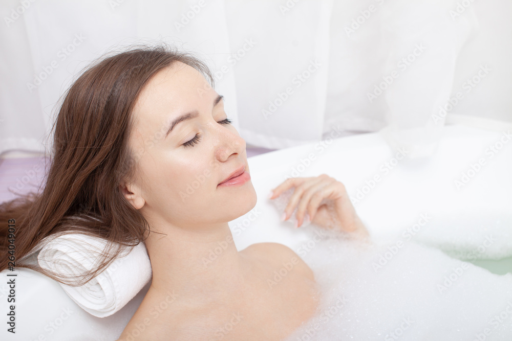 Young pretty woman relaxes in bathtube with soap foam. Spa procedures in bathroom at home or hotelroom. Skin care and moisturizing for youth preservation. Young pretty woman relaxes in bathtube with soap foam. Spa procedures in bathroom at home or hotelroom. Skin care and moisturizing for youth preservation.