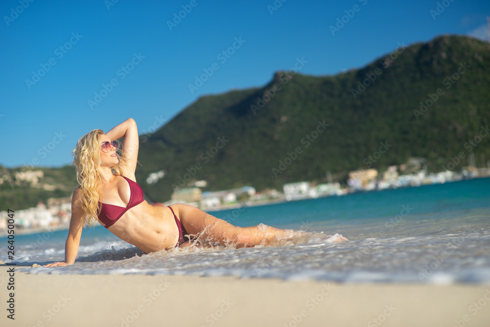 Naklejka premium Attractive blonde girl lying down on the beach, fit sporty healthy sexy body in bikini. Freedom, vacation, summertime fun concept