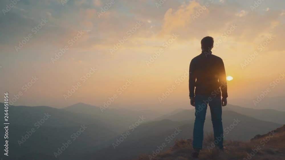 The man standing on the mountain against the sunset background The man standing on the mountain against the sunset background