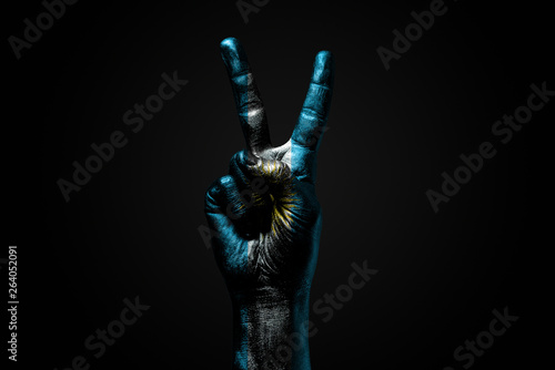 A hand with a drawn Argentina flag shows an PEACE sign, a symbol of peace, friendship, greetings and peacefulness on a dark background.