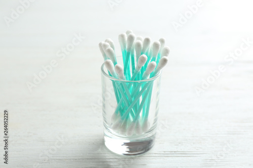 Glass with cotton swabs on white wooden background