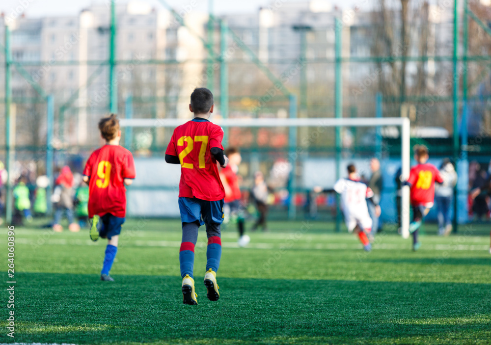 Obraz premium Boys at white red sportswear run, dribble, attack on football field. Young Soccer players with ball on green grass. Training, football, active lifestyle for kids