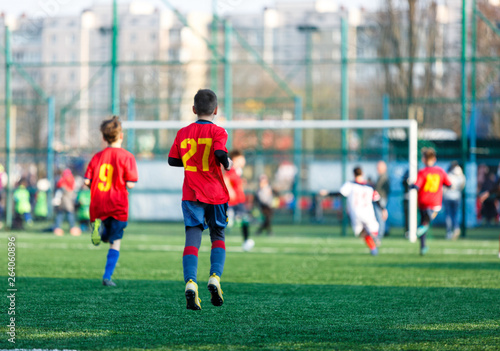 Boys at white red sportswear run, dribble, attack on football field. Young Soccer players with ball on green grass. Training, football, active lifestyle for kids 