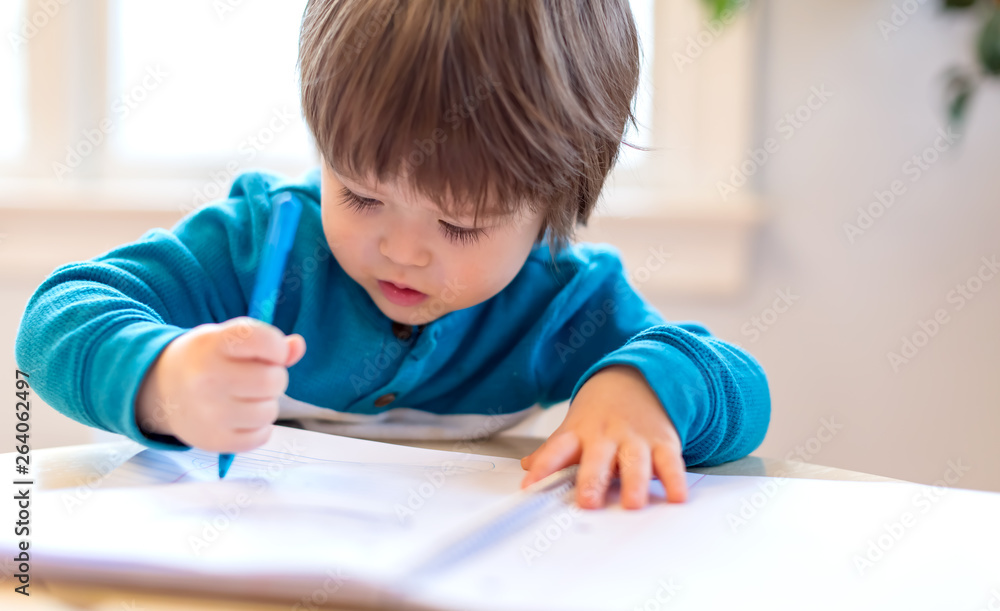 Toddler boy drawing with pen and paper at his desk Toddler boy drawing with pen and paper at his desk