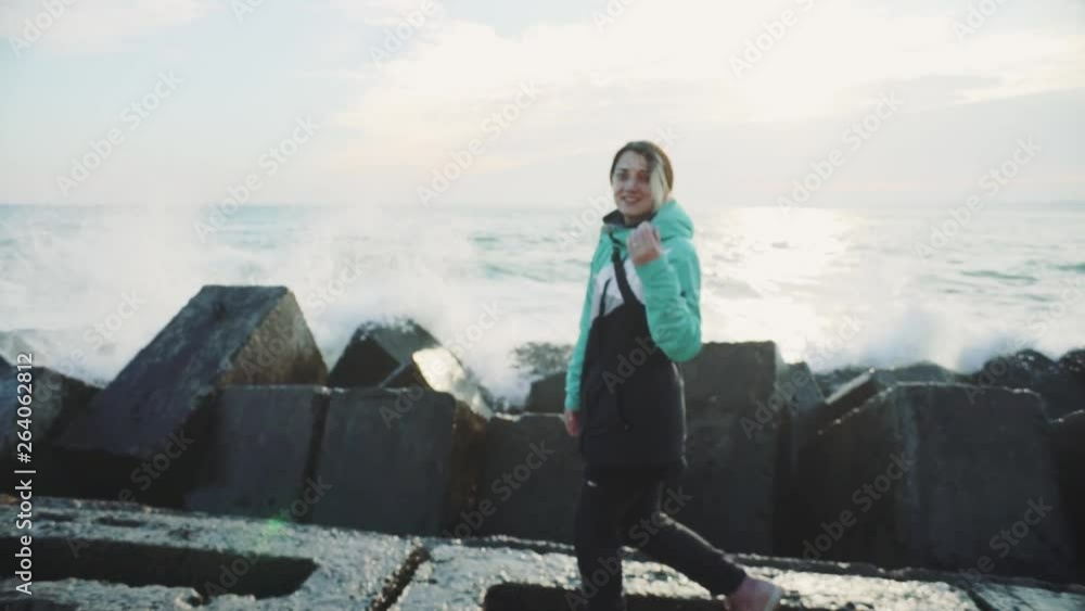 Attractive young woman in a warm jacket walking on the stone beach at sunset. Slow motion Attractive young woman in a warm jacket walking on the stone beach at sunset. Slow motion