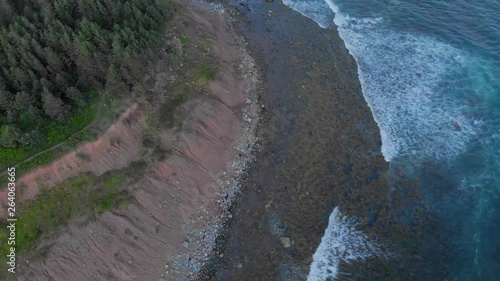 Cinematic drone / aerial footage moving forwards showing a road by the ocean, a forest and waves hitting the beach at Cole Harbour coast in Lawrencetown, Nova Scotia, Canada during summer season. photo