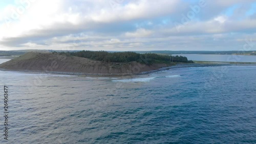 Cinematic drone / aerial footage rotating showing a road by the ocean, a forest and waves hitting the beach at Cole Harbour coast in Lawrencetown, Nova Scotia, Canada during summer season. photo