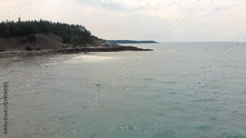 Cinematic drone / aerial footage moving forwards showing a forest, a bay and a couple of surfers in the cost of Kingsburg, Nova Scotia, Canada during summer season. photo