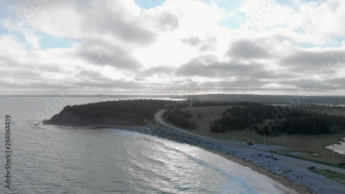 Cinematic drone / aerial footage descending showing a road by the ocean, a chalet and waves hitting the beach at Cole Harbour coast in Lawrencetown, Nova Scotia, Canada during summer season. photo