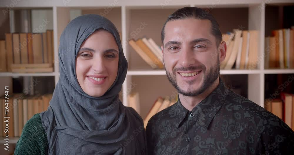 Closeup shoot of young muslim businesswoman and businessman looking straight at camera and smiling cheerfully indoors in the library Closeup shoot of young muslim businesswoman and businessman looking straight at camera and smiling cheerfully indoors in the library