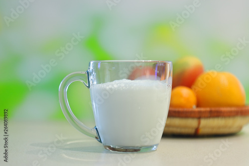 Fresh milk pouring into drinking glass with fruits in background