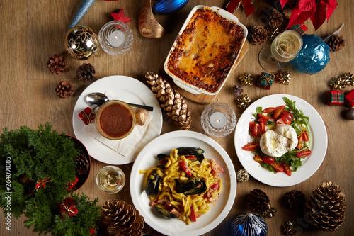 Flat lay of an Italian dinner table ready for Christmas celebration with some cooked lasagnas, a burrata salad, a dish of pasta, and a tiramisu