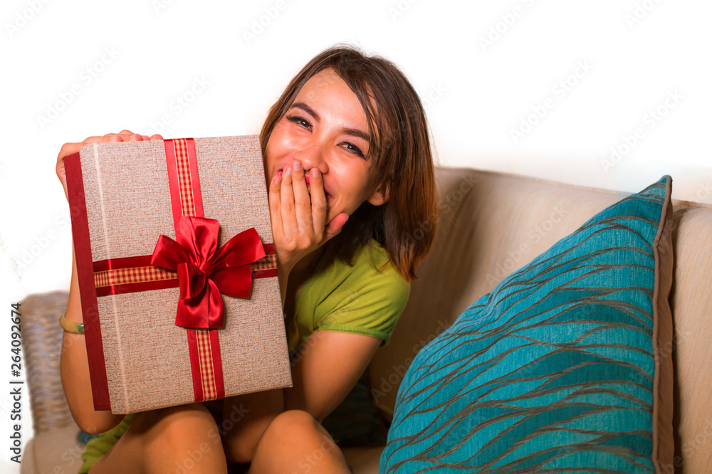 young beautiful and happy Asian Indonesian woman holding birthday or Christmas present showing the gift box cheerful and excited sitting on living room couch young beautiful and happy Asian Indonesian woman holding birthday or Christmas present showing the gift box cheerful and excited sitting on living room couch