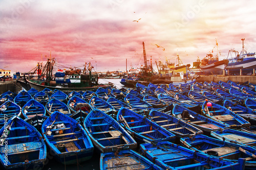 Scenic landscape with blue wooden fishing boats in the foreground in the port of Essaouira, Morocco during sunset