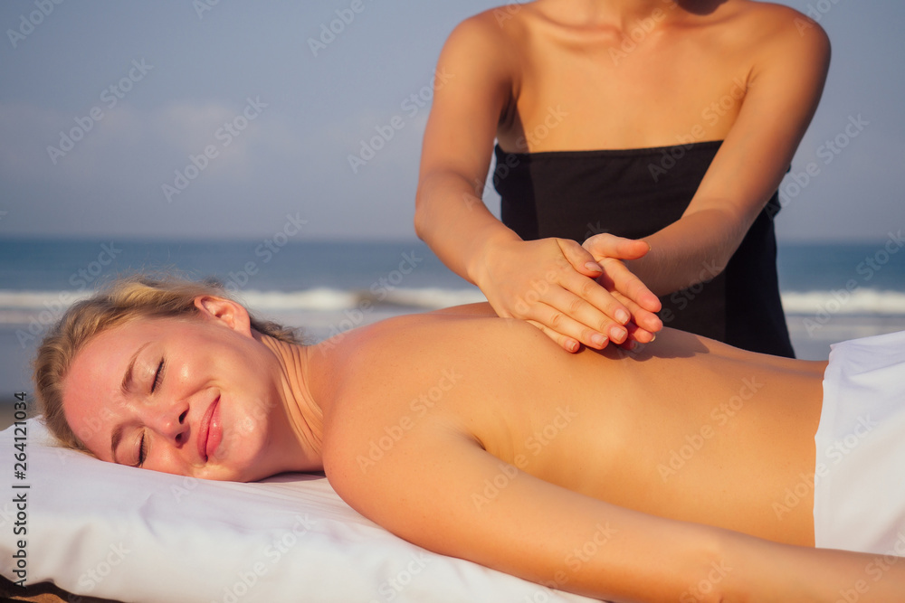 Obraz premium portrait of young beautiful woman on massage table beach morning getting spa on bach and sholders