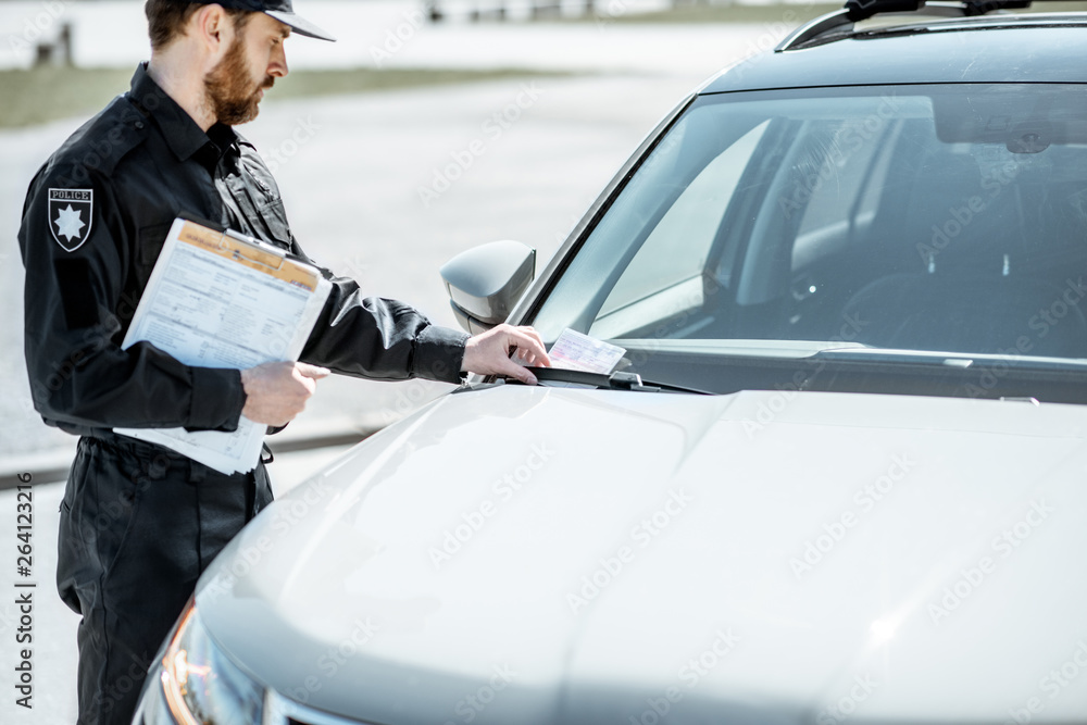 Policeman putting fine for improper parking on the windshield of the car on the roadside