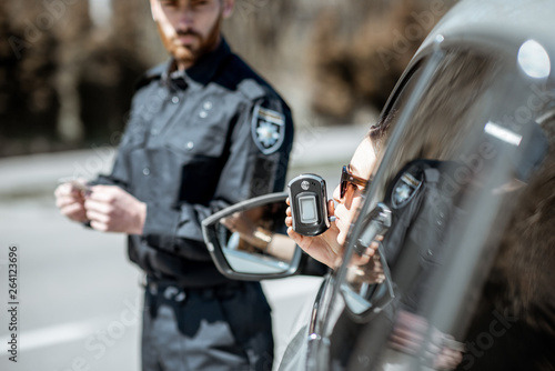 Policeman checking woman driver for alcohol intoxication with special device while stopped for violation traffic rules on the roadside
