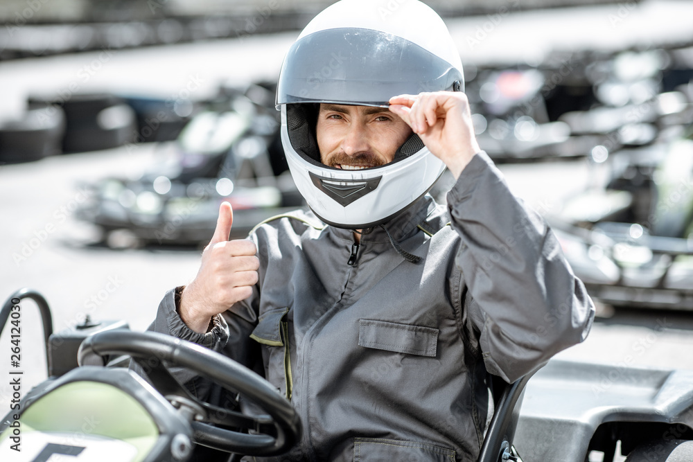 Portrait of a professional racer in sportswear and helmet sitting in the kart on the track Portrait of a professional racer in sportswear and helmet sitting in the kart on the track