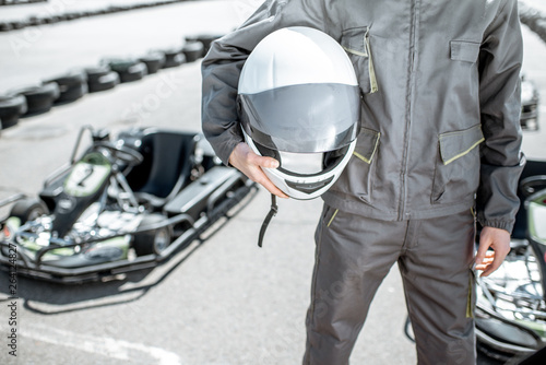 Racer holding protective helmet on the track with go-kart on the background