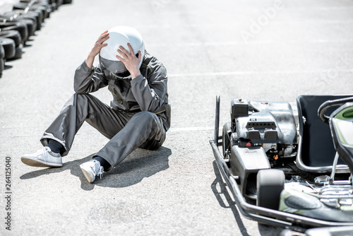 Despair racer in sportswear feeling sad lying on the track near the kart as a loser outdoors