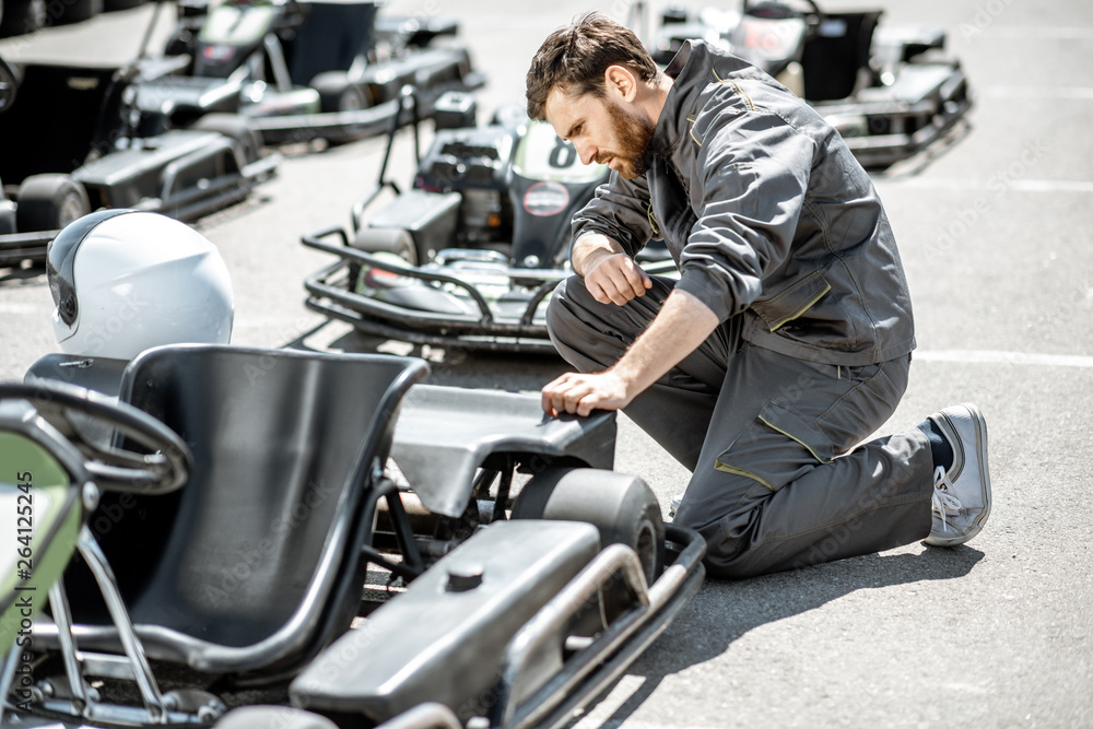 Racer or repairman in uniform serving go-kart machine before racing on the track Racer or repairman in uniform serving go-kart machine before racing on the track