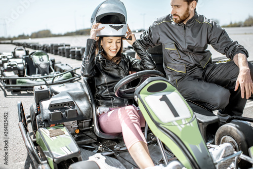 Instructor with happy young woman driver wearing protective helmet before the race on the go-kart track outdoors
