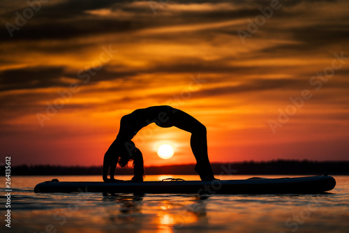 Young woman exercising on paddle-board at sunset.