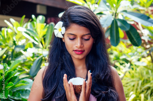 indian woman applying coconut oil dark brunette long hair in a hand on green summer park nature tropical