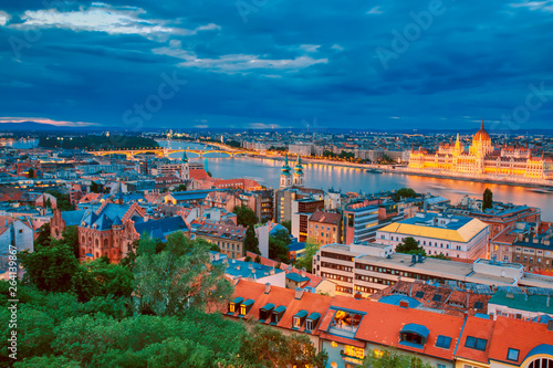 View of illuminated Parlament and riverside of Danube river in Budapest, Hungary during sunset with dramatic sky.