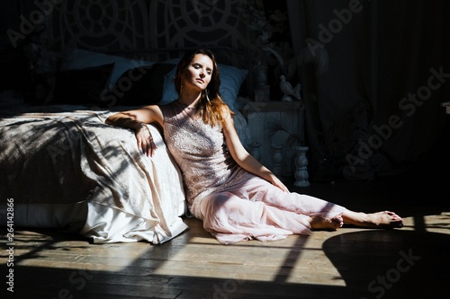 gorgeous young woman in luxurious dress sitting on the floor in bedroom