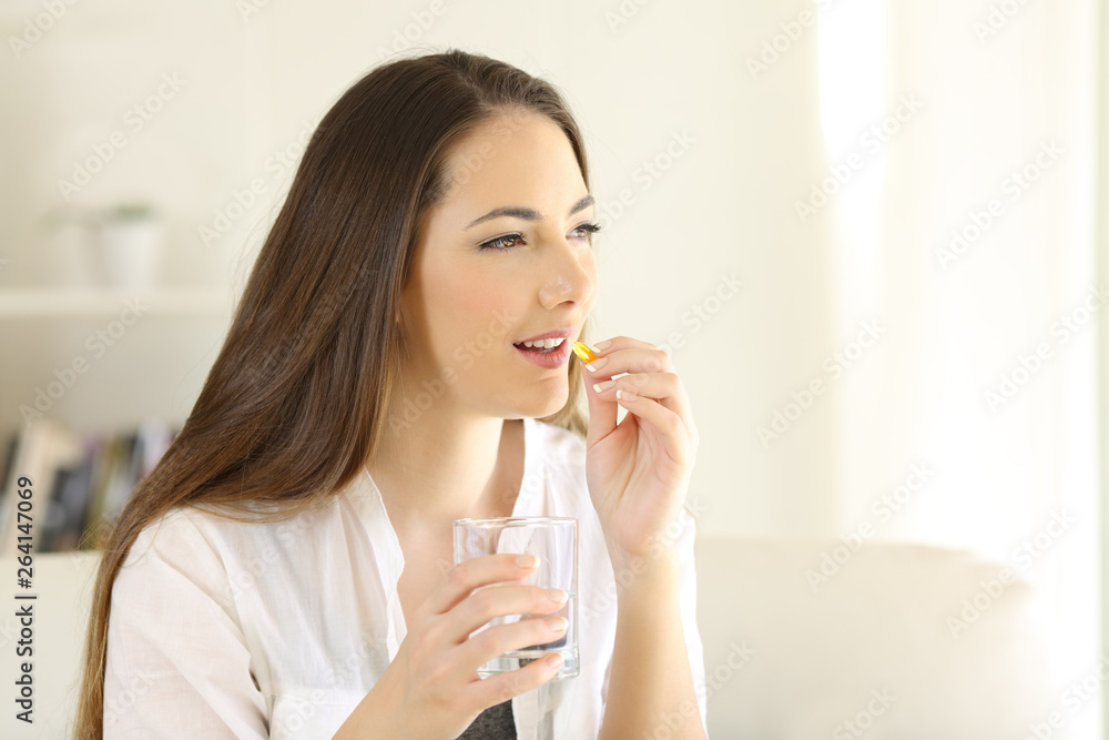 Happy woman taking vitamin pill holding glass at home Happy woman taking vitamin pill holding glass at home