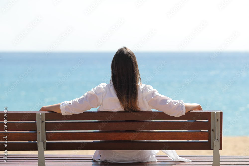 Happy woman watching the sea sitting on a bench