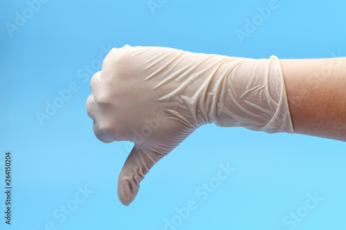 Fototapeta Naklejka Na Ścianę i Meble -  Fragment of a hand in white medical gloves that shows thumb down on a blue background. Show thumb down. Medical background