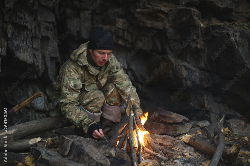 Man traveler kindled a fire to keep warm sheltered from the wind by the overhanging rock. Extreme travel. Survival in the wild. Man traveler kindled a fire to keep warm sheltered from the wind by the overhanging rock. Extreme travel. Survival in the wild.