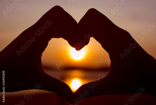 Silhouette hand forming a heart shape with sunrise in the middle and sea background, loving concept