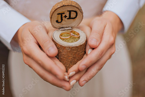 Wedding rings in a wooden box in a rustic style. The bride and groom are holding the box in their hands.