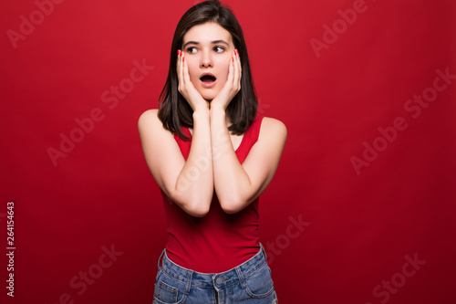 Portrait of happy surprised young woman standing isolated over red background. © dianagrytsku